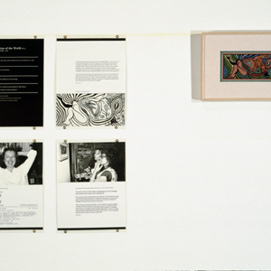 Four black and white panels with text and photographs hung in two rows on the left with framed petit point artwork, on the right