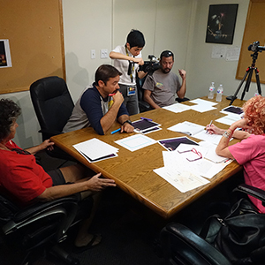 Color photograph of Mary Costa, Chris Souza, Marilyn Loddi, pyrotechnician Rusty Johnson, and Judy Chicago sitting and standing around a table in Pyro Spectaculars' conference room reviewing documents