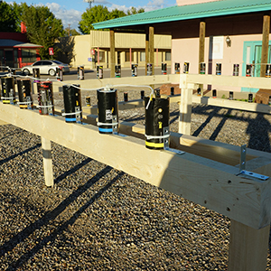 Color photograph of smoke canisters mounted on a rectangular wooden smoke test structure in a gravel lot with buildings and a street in the background