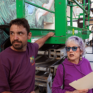 Color photograph of Judy Chicago and Chris Souza standing next to a green industrial lift