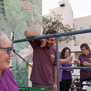 Color photograph of Judy Chicago and Chris Souza laughing with Gabriel Garcia, Vanessa Olvera, and Mary Costa on a scaffold