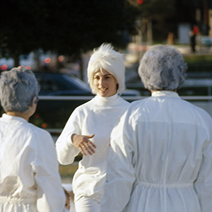 Color photograph of three adults dressed in white standing and talking with a child nearby amid stacks of white blocks