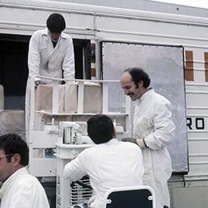 Color photograph of Lloyd Hamrol and three other people using a forklift to unload packages from a white truck