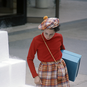 Color photograph of a young person holding a blue box standing next to a pyramid of white blocks