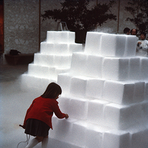 Color photograph of a young person holding a jump rope and touching a pyramid of white blocks
