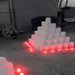 Color photograph of two pyramids of white blocks with red lights around them