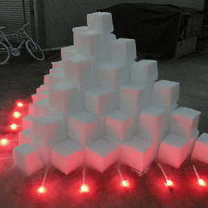 Color photograph of a pyramid of white blocks with red lights around it
