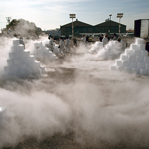 Color photograph of two rows of pyramids of white blocks with fog emanating from it and people standing around