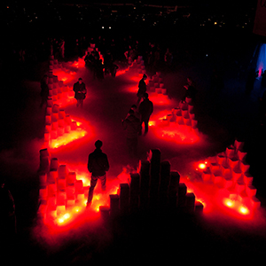 Color photograph, seen from above, of people standing among glowing red pyramids of blocks