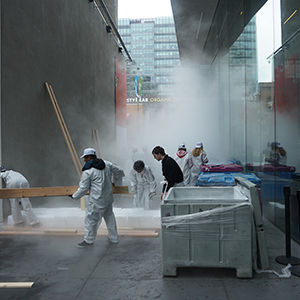 Color photograph of people installing white blocks of dry ice on the ground in a walkway between two buildings