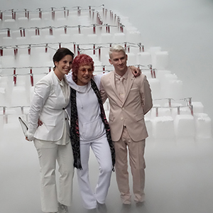 Color photograph of Jessica Silverman, Judy Chicago, and Samuel Zients standing in front of rows of white blocks of dry ice studded with red flares