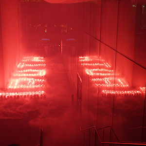 Color photograph of the word truth spelled out in blocks of dry ice lit with red flares and reflected in the glass of an adjacent building