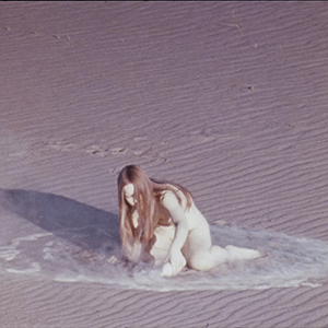 Color photograph of a nude woman kneeling in a puddle in the desert