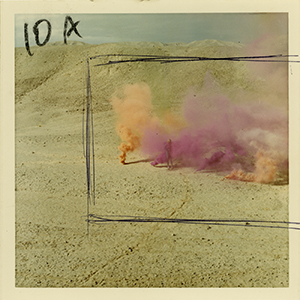 Color photograph of pink and orange smoke rising in the desert with annotation indicating cropping and 10A in black