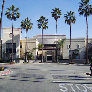 Color photograph of a large beige building with a red tiled roof and a line of palm trees in front