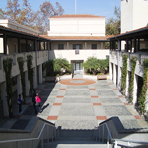 Color photograph of a courtyard with a patterned, tile floor inside a beige building with balconies and a red tiled roof