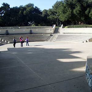 Color photograph of Judy Chicago and two other people standing inside a gray outdoor amphitheater