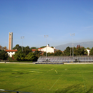 Color photograph of yellow caution tape strung across a sports field with bleachers and a tower in the background