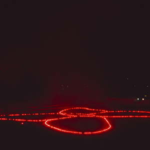 Color photograph of red flares in the shape of a butterfly on a dark ground