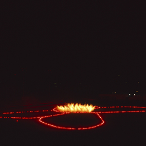 Color photograph of yellow fireworks at the center of red flares in the shape of a butterfly on a dark ground