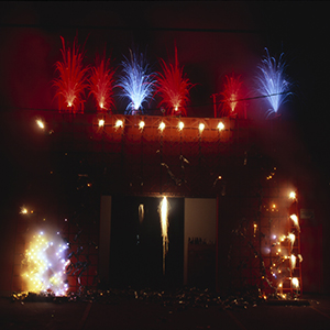 Color photograph of red, blue, and yellow fireworks on the facade of a building