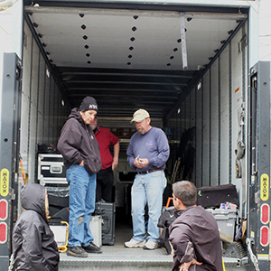 Color photograph of Chris Souza, Mary Costa, and three other people standing in the back of a truck with equipment in it