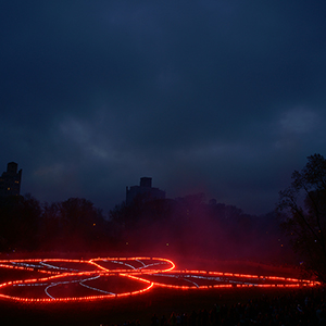 Color photograph of a glowing red butterfly outline with blue internal lines in a darkened park