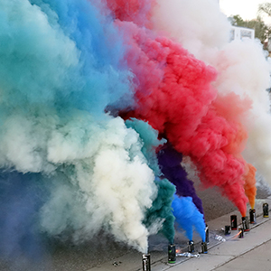 Color photograph of multicolored plumes of smoke emanating from flares on a curb