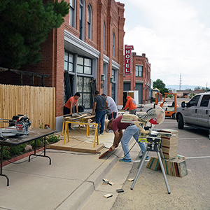 Color photograph of Ernesto Morales and four other people working with building supplies on the sidewalk outside a brick building